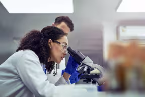 Scientist looking at test sample through microscope in laboratory