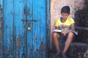 Child reading outside next to a locked door