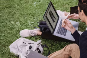 Two students sat on grass working from a laptop together. 