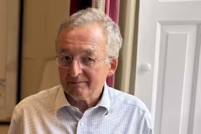 Professor Sir Dieter Helm standing in a room in New College, with a white window shutter and curtain behind him