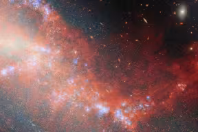 Image of a large red wispy structure in outer space connecting two galaxies seen as diffuse glows.