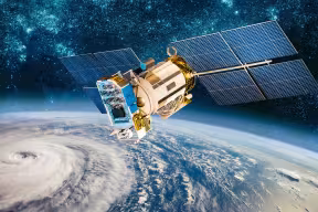 A satellite monitors a developing typhoon on Earth (seen as a spiral shaped cloud). Image credit: Shutterstock/ NASA