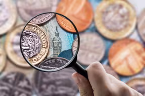 Magnifying glass over Big Ben surrounded by British currency