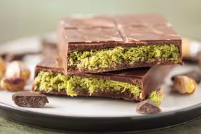 Close up of a chocolate bar snapped in two, on a plate. The bar is dark brown on the outside with a lurid green, crispy filling.