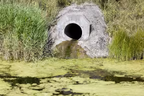 A wastewater pipe in a river bank dishcharges a stream of dirty water into a river. 
