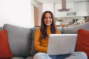 Young woman smiles at laptop while sitting on sofa
