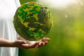 A person’s hands hold a green planet Earth as a symbol of sustainable development. 