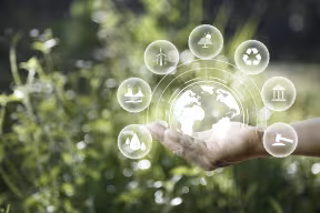 Green energy concept. Global warming-related icons (e.g. solar panel, recycling symbol) set on hands with a background of natural greenery.