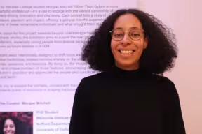 Portrait of Morgan Mitchell standing in front of her picture at the Other Than Oxford exhibition