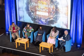 Aerial view of stage with panellists and moderator in discussion with Sheldonian Series graphic on a screen behind them