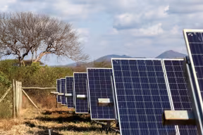 An array of solar panels standing upright on the ground in a rural area in Kenya.