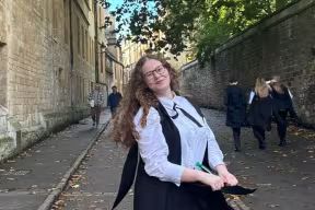 Daphne Harries stands, smiling, in sub fusc in Brasenose Lane