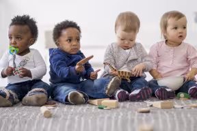 A multi-ethnic group of toddlers are sitting on the floor and are playing together with toys while on a play date.