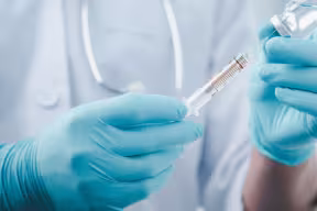 Doctor wearing gloves holding a vial of vaccine and syringe