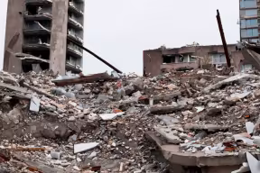 A building reduced to a pile of rubble, with ruined buildings in the background.