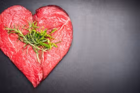 Photo | Heart shape raw meat with herbs on dark chalkboard background