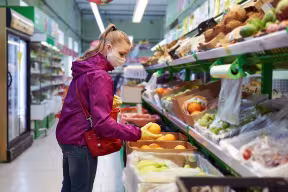 Woman in a supermarket looking at fruit wearing face mask