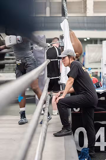 Julia Lee at ringside in a boxing gym, watching and coaching a boxer during training