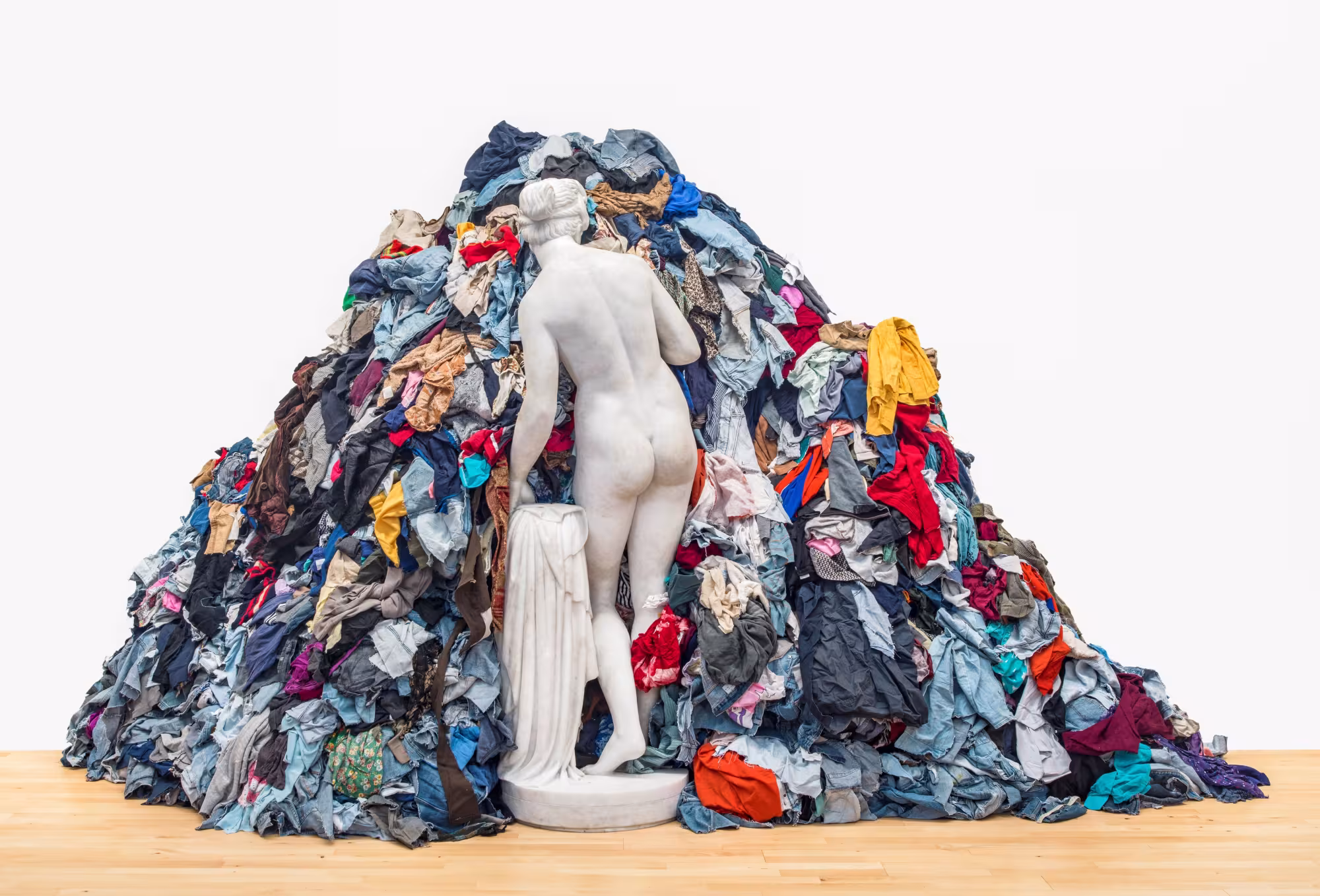Modern art installation of a nude Aphrodite-Venus statue facing into a pile of clothes of different colours.